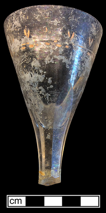 Colorless leaded stemmed glass. Conical/funnel shaped bowl and octagonal vertically fluted stem. Wheel engraved around rim and gold painted design. Rim diameter: 2.25”. This vessel falls into Bickerton’s (1986:20) Facet Cut Stem category (1760-1810). 18BC33
